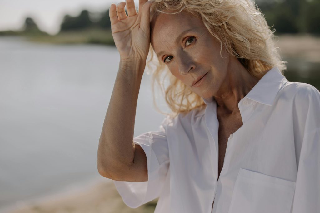 Portrait of a senior woman with blonde hair posing outdoors in sunlight.